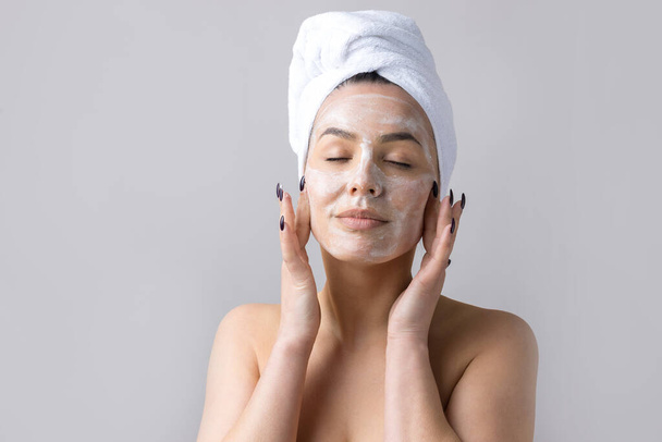 Schönheitsporträt einer Frau mit weißem Handtuch auf dem Kopf cremt das Gesicht ein. Reinigung der Haut Öko-Kosmetik Wellness-Entspannungskonzept. - Foto, Bild