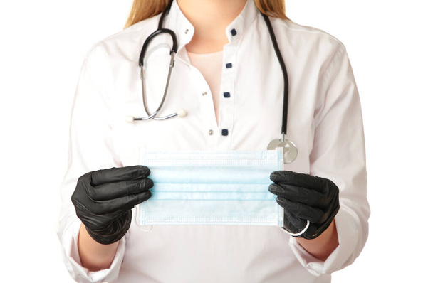 Orvos keze fekete kesztyűben orvosi védőmaszkot tart fehér alapon. Felülnézet - Fotó, kép