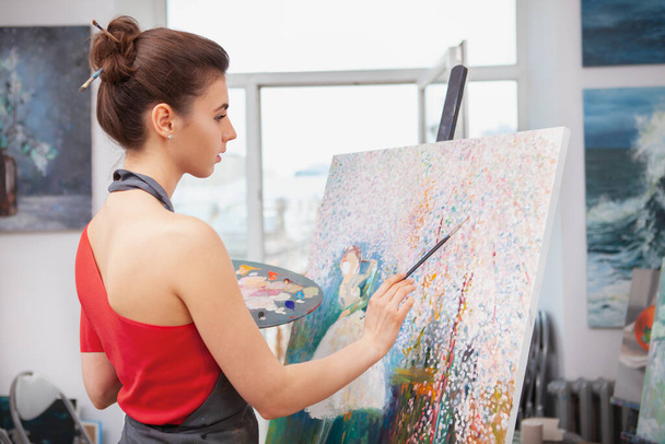Rear view shot of a young female artist working on a painting at her art studio - Фото, зображення