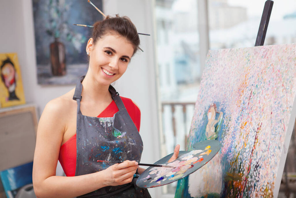 Happy beautiful woman smiling to the camera while painting at her workshop. Art, creativity concept - Фото, зображення