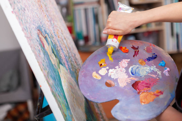 Close up de um artista espremendo tinta a óleo amarelo em uma paleta enquanto trabalhava no estúdio de arte
 - Foto, Imagem
