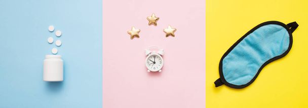 ピンク、黄色、青の芸術の背景に星と丸薬、ボトル、睡眠マスクと白い目覚まし時計。概念不眠症,睡眠の問題,薬や治療を受ける時間.トップビュー、フラットレイアウト、コピースペース. - 写真・画像