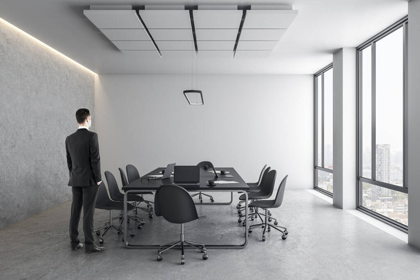 Businessman standing in concrete office interior with city view, daylight, furniture and equipment. - Foto, afbeelding