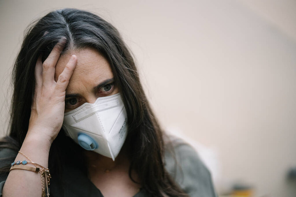 Coronavirus (COVID-19. Portrait of sad and worried young woman wearing a face mask for virus protection touching her worried head. Epidemic and pandemic concept - Fotó, kép