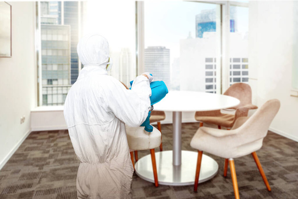 Hombre con un traje protector blanco rociando desinfectante en la habitación de la oficina. Prevenir la propagación de la gripe Coronavirus
 - Foto, imagen