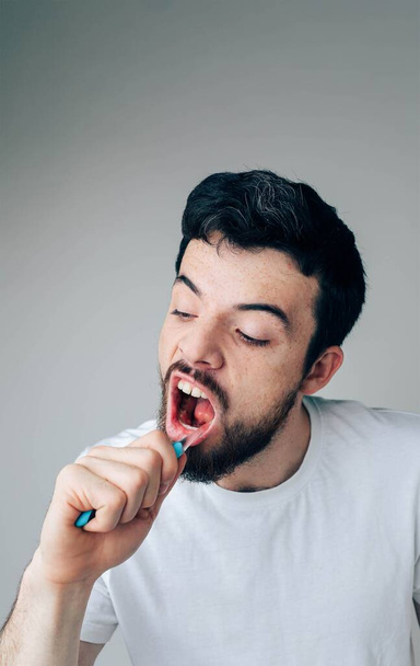 Young man isolated over background. Hardworking serious guy cleaning teeth with toothbrush. Take care of oral and dental health. Vertical picture and close up photo - Fotografie, Obrázek