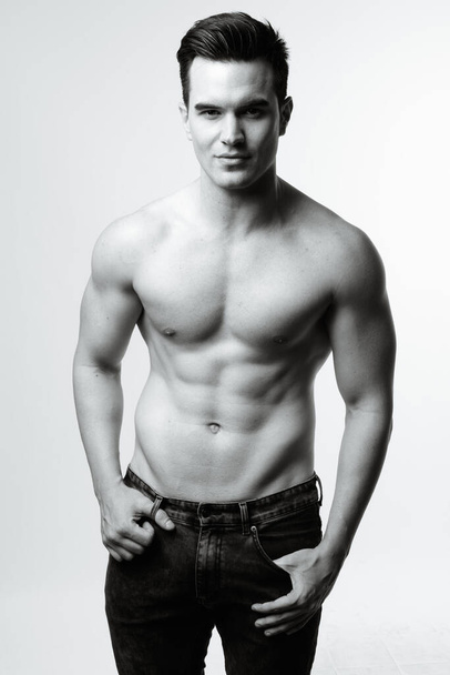 Studio shot of young handsome muscular man shirtless against white background in black and white - Foto, afbeelding