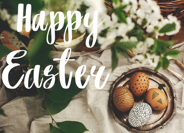 Hyvää pääsiäisviestiä. Pääsiäistervehdys. Luonnollinen pääsiäismunia maalattu vahalla vintage levy ja paju kori, valkoinen kevät kukkia puinen pöytä. Tervehdyskortti
 - Valokuva, kuva