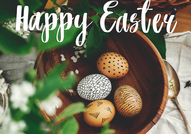 Hyvää pääsiäisviestiä. Pääsiäistervehdys. Luonnollinen pääsiäismunia maalattu vahalla puinen kulho ja paju kori, valkoinen kevät kukkia puinen pöytä. Ekolomalle. Tervehdyskortti
 - Valokuva, kuva