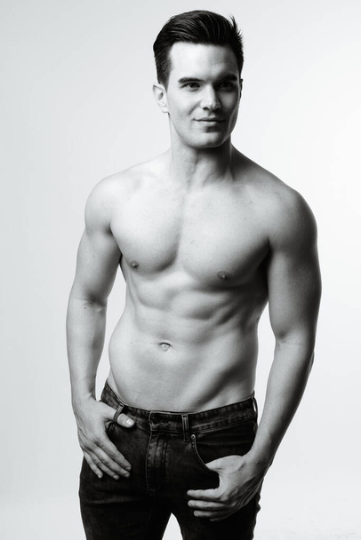 Studio shot of young handsome muscular man shirtless against white background in black and white - Photo, image