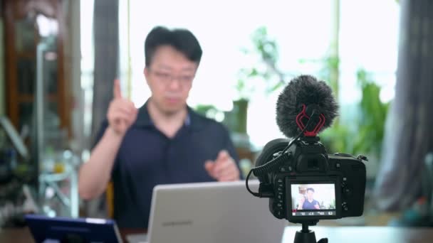 Online előadás koncepció. Ázsiai középkorú férfi online előadásokat tart otthon. Homályos háttér. - Felvétel, videó