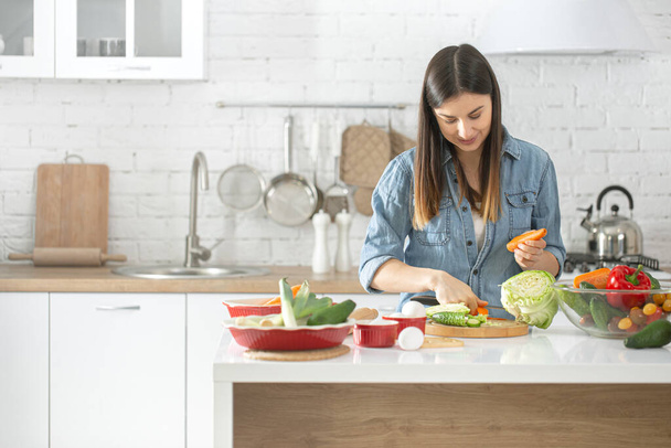 Nuori kaunis nainen valmistaa salaattia erilaisista vihanneksista keittiössä. Terveellisen ruokavalion ja elämäntavan käsite. - Valokuva, kuva
