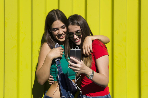 Молоді жінки з щасливим обличчям проти зеленої стіни слухають музику на навушниках і отримують задоволення
 - Фото, зображення