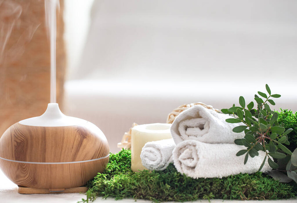 Spa composition with the aroma of a modern oil diffuser with body care products . Twisted white towels, spring greens and flowers. Spa concept for body and health care . - Photo, Image