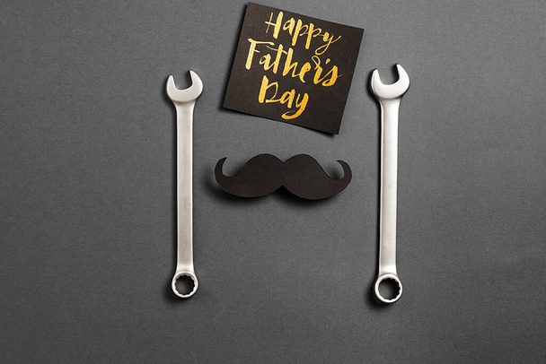 Creative flat lay composition with combination wrenches, card with phrase happy father's day and retro stylish black paper photo booth props moustaches on grey background. Space for text - Fotografie, Obrázek