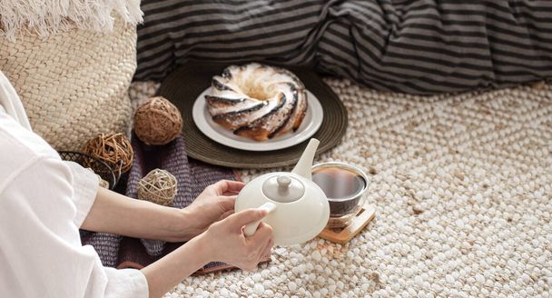 若い女性の手がティーポットからお茶を注ぐ。居心地の良い家庭的な雰囲気の中で朝食を準備. - 写真・画像