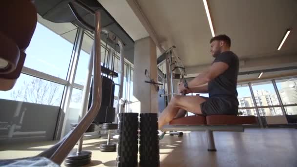 Knappe jonge man met behulp van zittende rij machine in de sportschool - Video