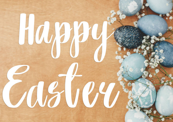 Happy Easter text. Easter greetings lettering. Flowers and modern Easter eggs flat lay on rustic wood. Stylish pastel blue eggs border. Greeting card - Fotografie, Obrázek