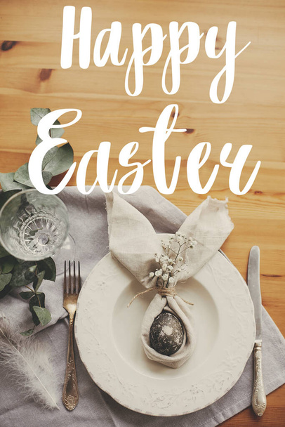 Happy Easter text. Easter greetings lettering. Stylish Easter egg in bunny ears napkin on rustic table, flat lay. Modern marble egg. Holiday table decorations. Greeting card - Φωτογραφία, εικόνα
