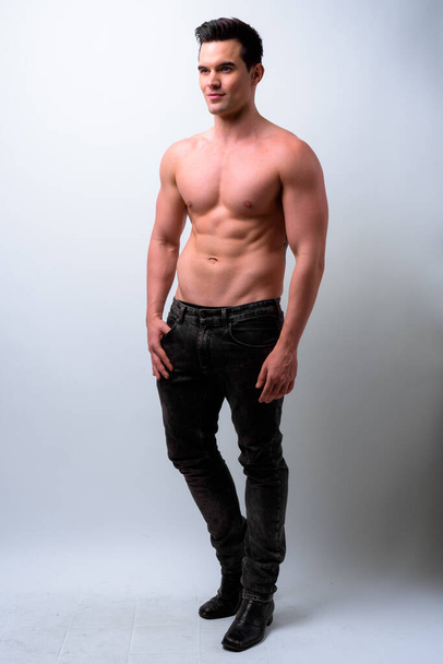 Studioaufnahme eines jungen, gut aussehenden, muskulösen Mannes ohne Hemd vor weißem Hintergrund - Foto, Bild