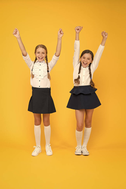 Celebrating back to school. Happy girls celebrating achievement in study on yellow background. Small cute schoolchildren celebrating and making winner gestures. Keep celebrating school holidays - Photo, image