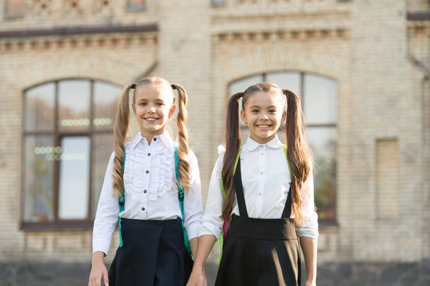 Lucky to meet each other. Cheerful smart schoolgirls. Happy schoolgirls outdoors. Small schoolgirls wear school uniform. Cute schoolgirls with long ponytails looking charming. Ending of school year - Фото, изображение