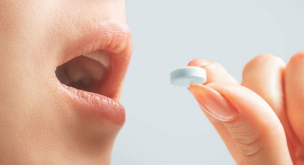 Young woman taking a medical white round pill, close-up of mouth and hand. - Photo, image