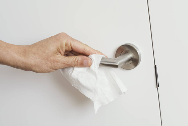 primer plano de un hombre caucásico limpiando la manija de la puerta con una toallita desinfectante
 - Foto, imagen