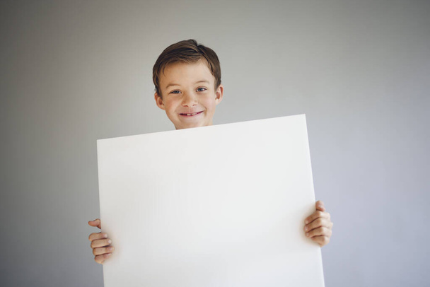 cool young boy holding white empty sheet in front of grey background  - Foto, immagini
