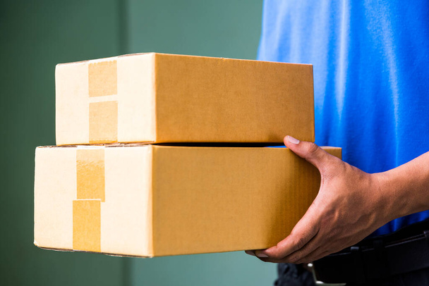 Close up Delivery man in blue uniforms holding parcel cardboard box. - Foto, afbeelding