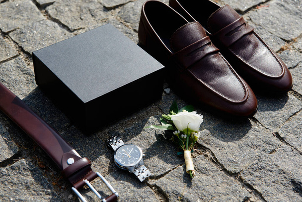 Close up of brown male shoes, belt, watches and boutonniere on stone background, copy space. Modern man accessories. Wedding details - Fotografie, Obrázek