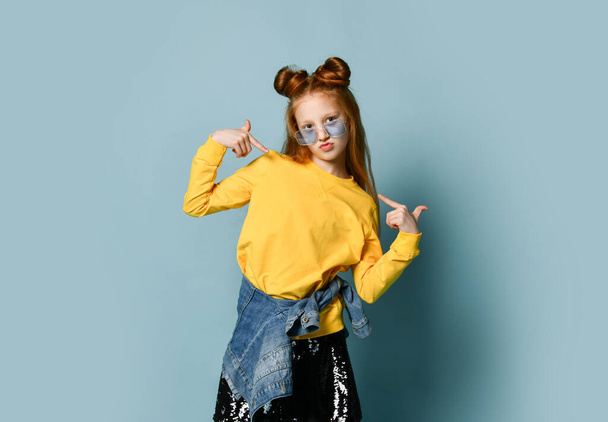 Teenager girl in yellow sweatshirt and black skirt poses as a top model pointing fingers at herself with both hands - Fotó, kép