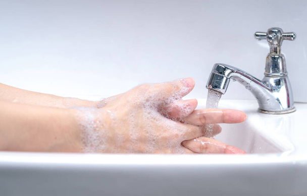 Kobieta myje ręce pianką mydlaną i wodą z kranu w łazience. Ręcznie czyste pod kranem na zlewie dla higieny osobistej, aby zapobiec grypie i koronawirusowi. Dobra procedura mycia rąk, aby zabić bakterie, wirus. - Zdjęcie, obraz