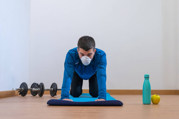 Coronavirus. COVID-19. Young man doing sport at home during quarantine with mask protection. Stay at home activities. prevent infection from the pandemia. Healthy at home.  - 写真・画像