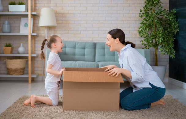 Mother and daughter are unpacking cardboard box at home.                                 - Zdjęcie, obraz
