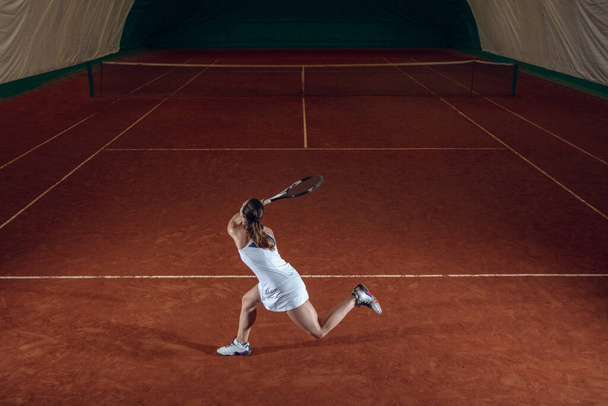Young caucasian professional sportswoman playing tennis on sport court background - 写真・画像