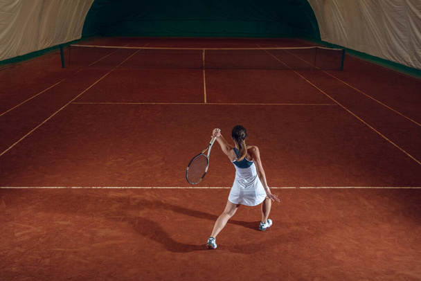 Молодая кавказская профессиональная спортсменка, играющая в теннис на спортивном фоне
 - Фото, изображение