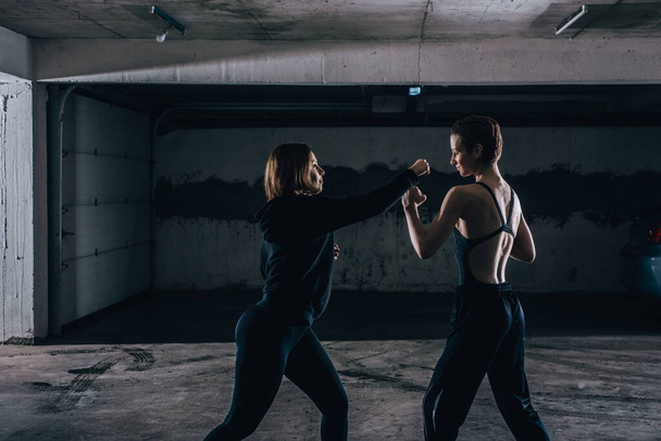 Silhouette de deux jeunes femmes pratiquant le combat à l'intérieur du garage. - Photo, image