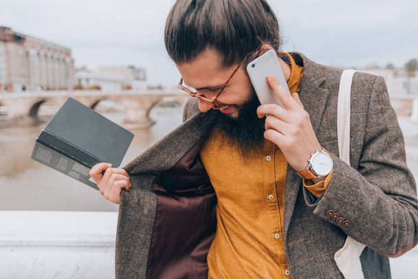 Elegante hombre hipster con ropa de moda durante una conversación telefónica en un entorno urbano - Foto, Imagen