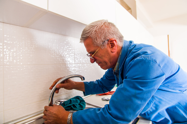 Reparador está trabalhando duro com sua ferramenta na cozinha e consertar a torneira da cozinha
 - Foto, Imagem