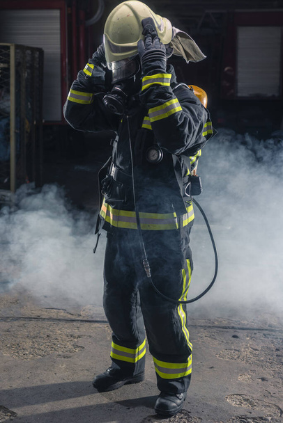 Портрет пожежника з вогнепальними гарматами та шоломом. Темний фон з димом і синім світлом
. - Фото, зображення
