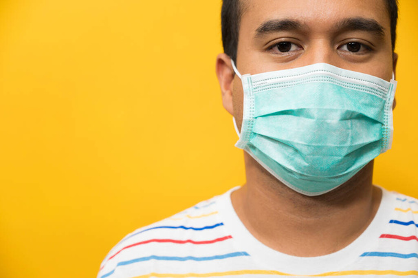 Close up joven asiático hombre usando protección cara máscara contra coronavirus en amarillo fondo
. - Foto, imagen