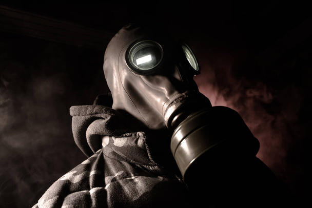 Desastre ambiental. Sobrevivente pós-apocalíptico com máscara de gás num fundo escuro. Retrato dramático de um homem com uma máscara de gás. Meios de protecção contra radiações. Foco seletivo
 - Foto, Imagem