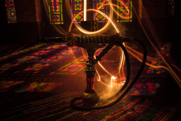 Ζεστά κάρβουνα σε μπολ shisha δημιουργώντας σύννεφα ατμού στο εσωτερικό της Αραβίας. Ένα ανατολίτικο στολίδι στο χαλί. Κομψό ανατολίτικο shisha στο σκοτάδι με backlight. - Φωτογραφία, εικόνα