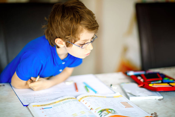 Ahkera onnellinen koulupoika tekee läksyjä karanteeniaikana koronapandemiasta. Terve lapsi kirjoittaa kynällä, jää kotiin. Kotikoulun käsite - Valokuva, kuva