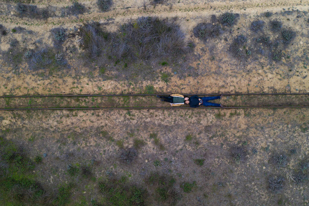 Couple lying on a rail track drone aerial top view on a desert landscape - Foto, imagen