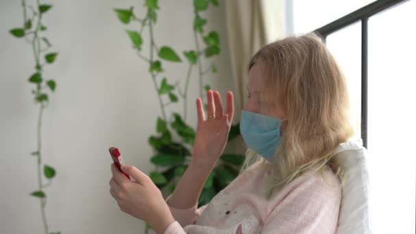 Καραντίνα για την επιδημία του κορωνοϊού. Μια μολυσμένη γυναίκα με μάσκα συνομιλεί μέσω βίντεο σε ένα smartphone. - Πλάνα, βίντεο