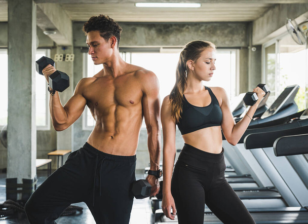 Homem de fitness e mulher segurando halteres posando perto da esteira. Treinamento de casal muscular no ginásio
. - Foto, Imagem