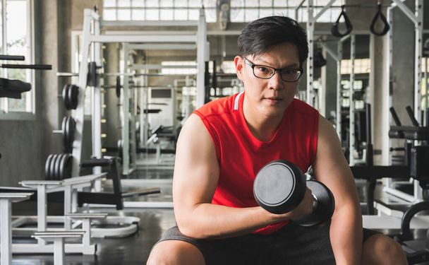 Güçlü kaslı Asyalı adam spor salonunda bisepslerde egzersiz yapıyor. Ağırlık antrenmanı konsepti. - Fotoğraf, Görsel