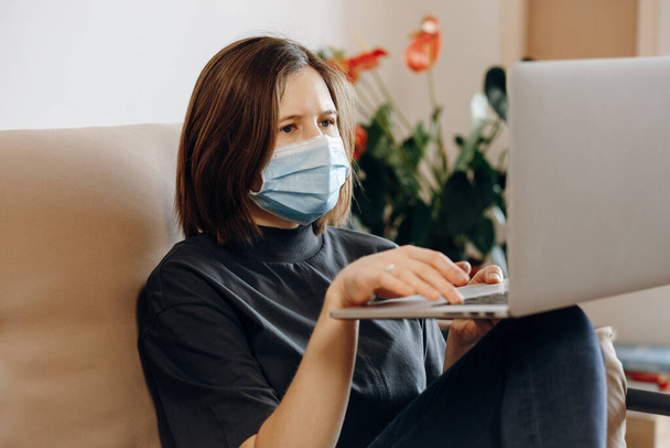 Girl studing remotely at home with laptop, online training education. Protective mask on face. Social isolating, quarantine, lifestyle, stay home concept.Coronavirus pandemic - Photo, Image